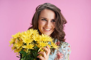 Portrait of happy modern female in floral dress with yellow chrysanthemums flowers isolated on pink background.