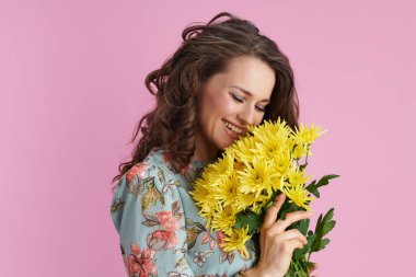 smiling modern female with long wavy brunette hair with yellow chrysanthemums flowers against pink background.