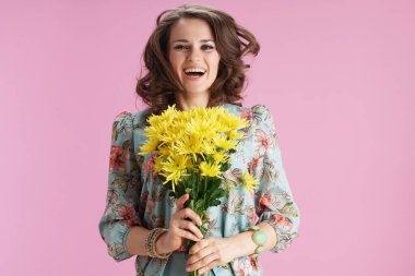 smiling trendy female in floral dress with yellow chrysanthemums flowers jumping isolated on pink background.