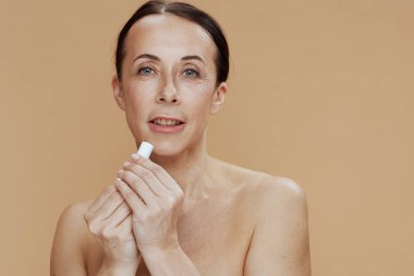 modern middle aged woman with hygienic lipstick on beige background.