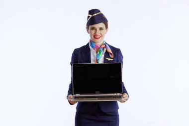 smiling modern female stewardess isolated on white background in uniform showing laptop blank screen.