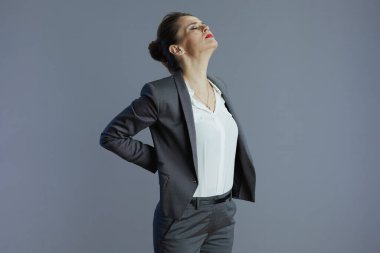 tired young woman worker in grey suit having back pain isolated on grey background.