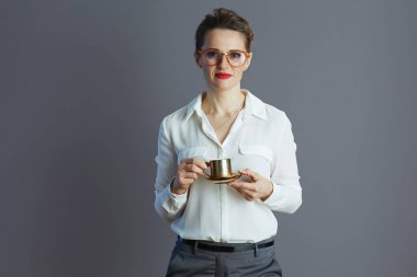 modern female employee in white blouse with glasses and coffee cup on grey.