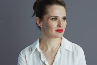 pensive middle aged business woman in white blouse looking at copy space on gray background.