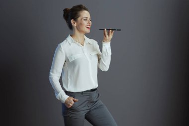 smiling trendy 40 years old small business owner woman in white blouse talking on a smartphone on grey.