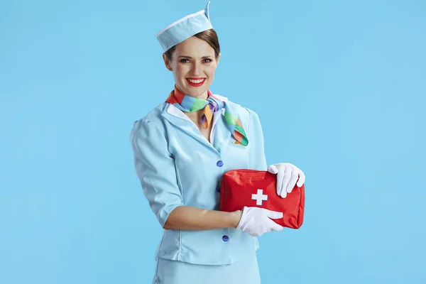 smiling modern air hostess woman on blue background in blue uniform with first aid kit.