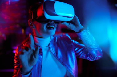 Neon metaverse futuristic concept. smiling modern woman in virtual reality goggles exploring metaverse in modern office.