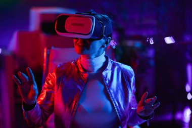 Neon metaverse futuristic concept. happy trendy 40 years old woman in virtual reality goggles in modern office create project in virtual reality.