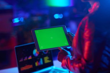 Seen from behind modern business woman with digital tablet and green screen in modern office.