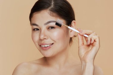 Portrait of modern woman with brow brush isolated on beige background.