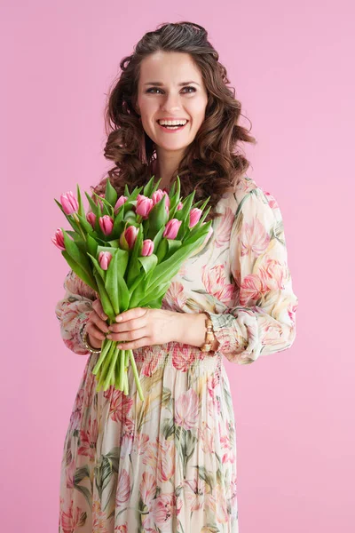 幸せなエレガントな女性とともに長いです波状ブルネット髪とともにチューリップ花束とともにピンクの背景 — ストック写真