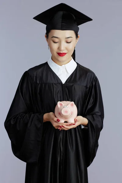 Young Female Asian Graduate Student Piggy Bank Isolated Grey Background — Stockfoto