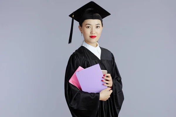 modern female asian graduate student with books and notebooks isolated on gray.
