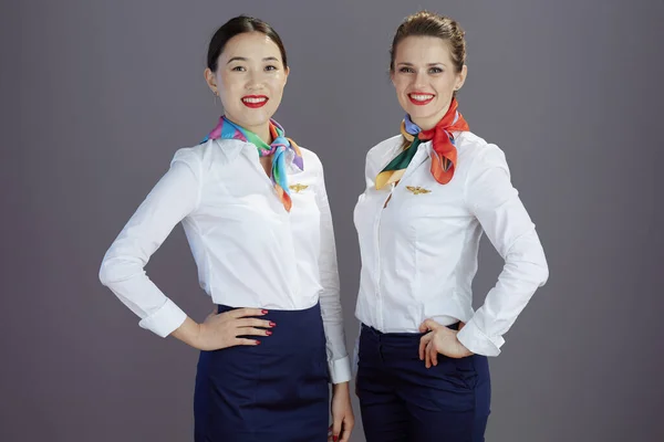 smiling stylish stewardess women in blue skirt, white shirt and scarf isolated on gray background.