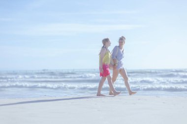 Sahilde yürürken gülümseyen zarif anne ve çocuğun tam boy portresi..