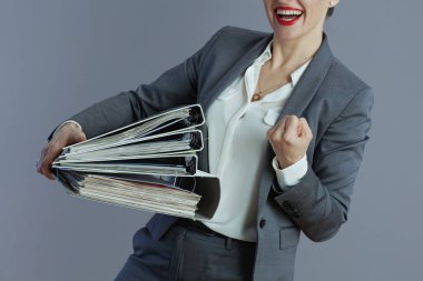 Gri takım elbiseli orta yaşlı küçük işletme sahibi bayana yakın plan. Gri renkli klasörler sevinçle izole edilmiş..