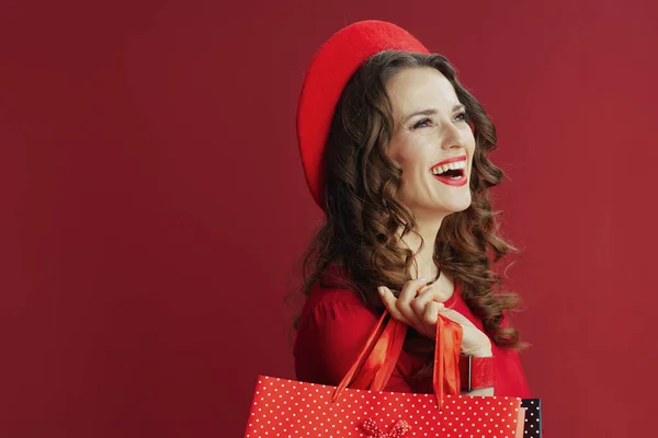 ハッピーバレンタイン 幸せな現代的な中年女性で赤のドレスとベレー帽隔離された赤の背景にショッピングバッグ — ストック写真