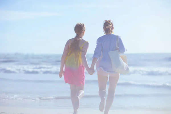 ビーチで走っている現代の母親と十代の娘の後ろから見た — ストック写真