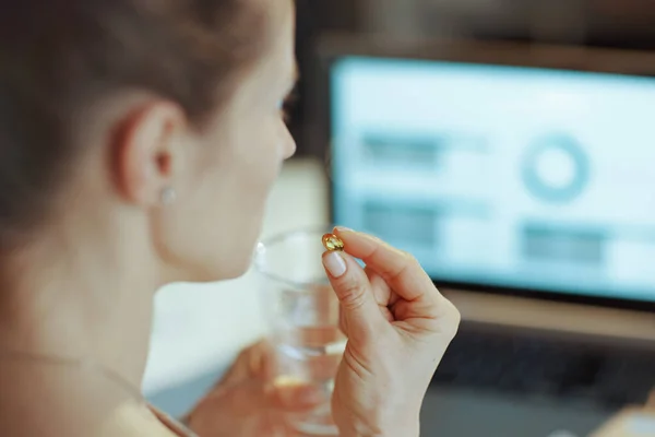 Closeup on modern woman with laptop, pills and glass of water in modern office.