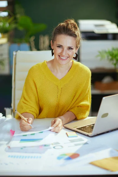 在现代绿色办公室里 穿着黄色毛衣 拿着文件工作的现代小企业主女人微笑着 — 图库照片