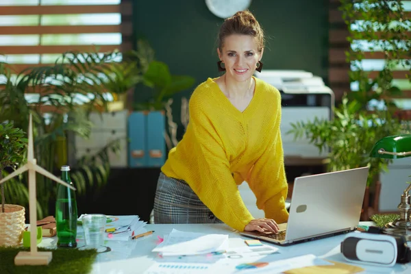 スタイリッシュな中年中小企業経営者女性で黄色セーターでラップトップスタンドでザ 現代緑のオフィス — ストック写真