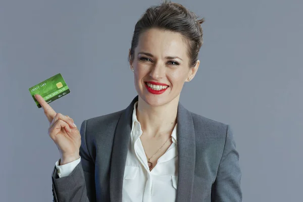 笑顔の現代的な中年女性労働者でグレースーツクレジットカードで隔離されたグレー — ストック写真