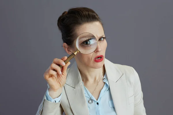 スタイリッシュな中年中小企業経営者女性ですライトビジネススーツで虫眼鏡でグレーの背景に隔離 — ストック写真