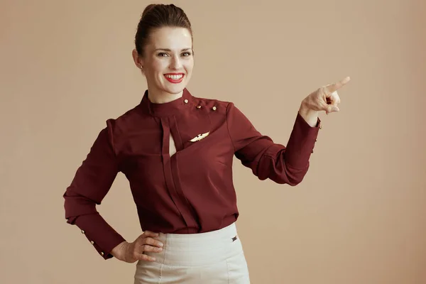 コピースペースを指しているベージュの背景に対する幸せな現代の女性客室乗務員 — ストック写真