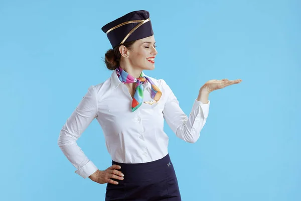 Uśmiechnięta Elegancka Stewardessa Niebieskim Tle Mundurze Prezentująca Coś Pustej Dłoni — Zdjęcie stockowe