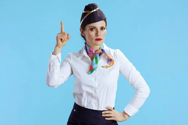 elegant air hostess woman isolated on blue background in uniform with raised finger drawing attention.