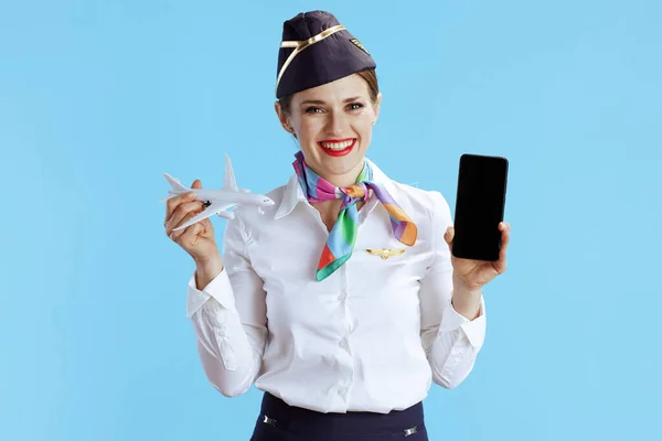 快乐优雅的女空姐 蓝色背景 身穿制服 显示智能手机空白屏幕 — 图库照片