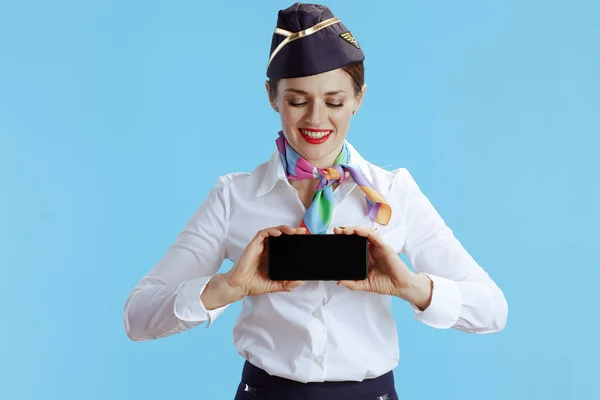 在蓝色背景下穿着制服微笑优雅的空姐 展示智能手机空白屏幕 — 图库照片