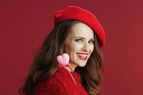 ハッピーバレンタイン 笑顔トレンディーな中年女性で赤いセーターとベレー帽でハートオンスティック — ストック写真