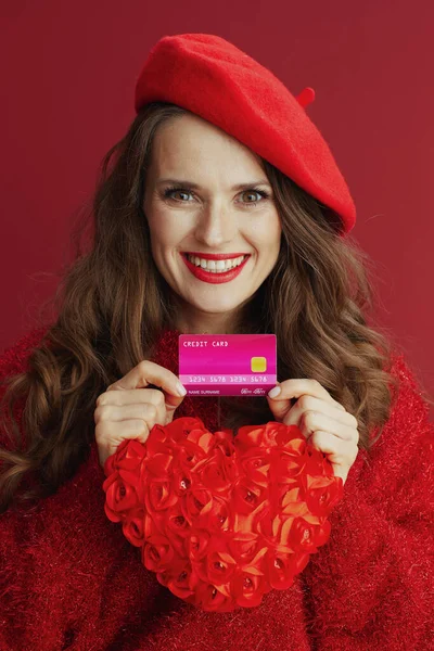 ハッピーバレンタイン 幸せな流行の女性で赤いセーターとベレー帽で赤いハート 長い波状の髪とクレジットカード — ストック写真