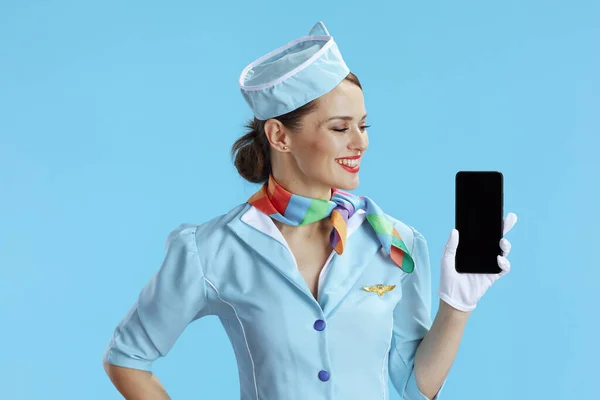 穿着蓝色制服的优雅的空姐 蓝色背景 显示智能手机空白屏幕 — 图库照片