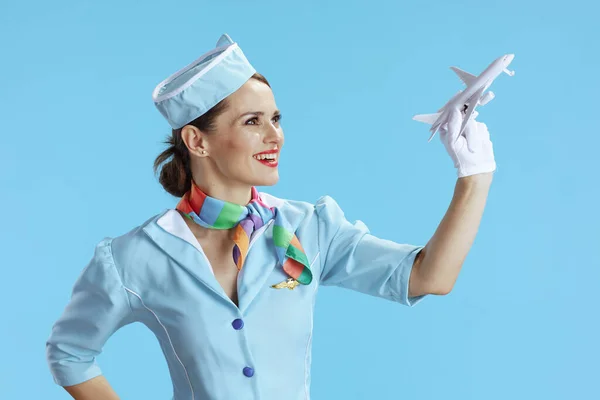 smiling modern female air hostess isolated on blue background in blue uniform with a little airplane.