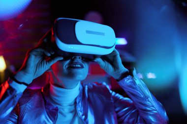 Neon metaevren fütüristik konsepti. Karanlık arka planda sanal gerçeklik gözlüklü meraklı modern kadın..