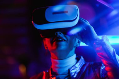 Neon metaverse futuristic concept. modern middle aged woman in virtual reality goggles on dark background.