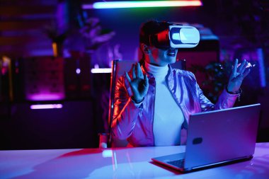 Neon metaevren fütüristik konsepti. Sanal gerçeklik gözlüklü mutlu orta yaşlı kadın modern ofiste sanal gerçeklik tasarlıyor..