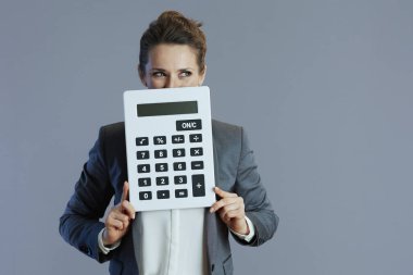 Gri arka planda hesap makinesi olan 40 yaşında, gri takım elbiseli bir kadın..