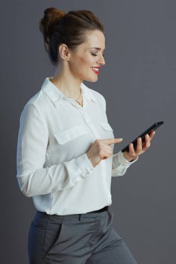 Beyaz bluzlu, güler yüzlü bayan çalışan gri üzerinde izole akıllı telefon kullanarak mesajlaşıyor..