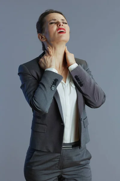 穿着灰色西装的40岁的小企业主女人 在灰色背景下脖子酸痛 — 图库照片