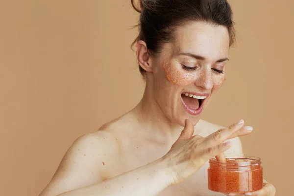 happy modern woman with face scrub isolated on beige.