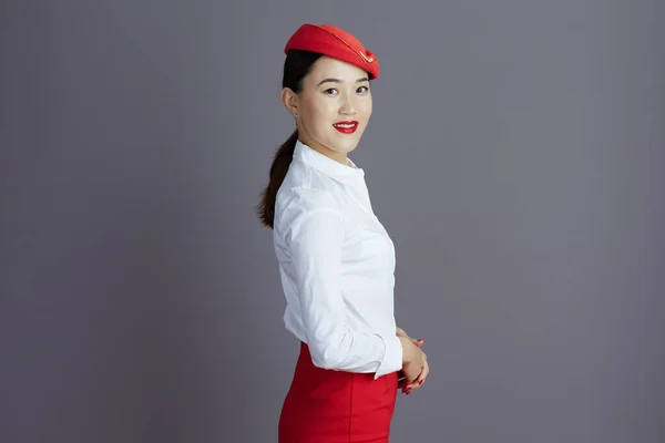 Улыбающаяся Элегантная Азиатская Стюардесса Красной Юбке Шляпе Изолированная Сером Фоне — стоковое фото
