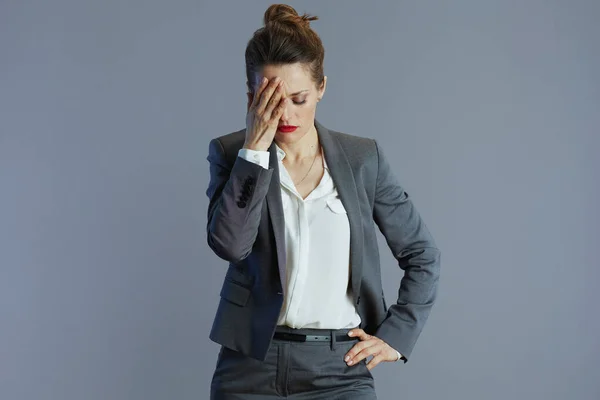 stressed stylish 40 years old woman employee in gray suit isolated on gray background.