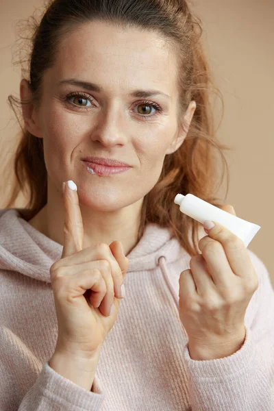 ベージュで隔離された指を使用して軟膏を適用するチューブの唇と軟膏のヘルペスを持つ女性 — ストック写真