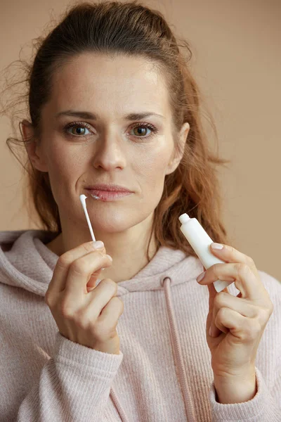 40歳の女性とともにヘルペス唇に軟膏を適用綿棒を使用してベージュの背景に対して — ストック写真