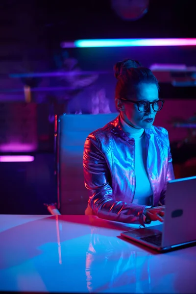 未来的な概念を嫌悪するネオン 現代のオフィスにノートパソコンを持つ眼鏡の高価な流行の女性 — ストック写真