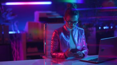 Neon metaevren fütüristik konsepti. Modern ofiste dizüstü bilgisayarı ve akıllı telefonu olan 40 yaşında modern bir kadın..