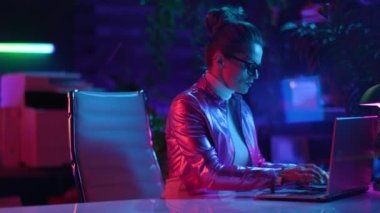 Neon metaevren fütüristik konsepti. Modern ofiste dizüstü bilgisayarlı gözlüklü şık orta yaşlı kadın..